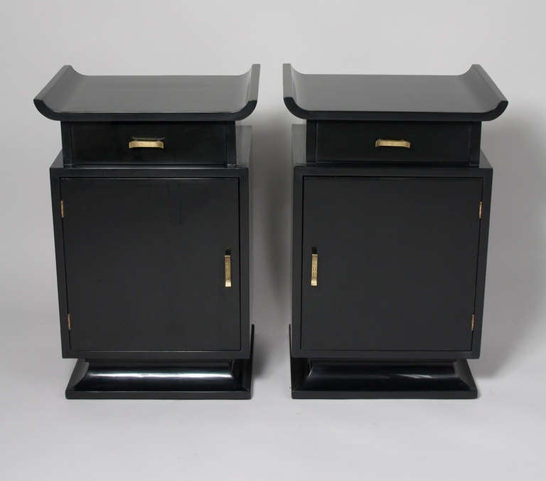 Pair of black lacquered Asian Modern nightstands or end tables, the top surface having upturned sides, with a single drawer over a door concealing a storage compartment, on tapered plinth base with textured bronze pulls, by James Mont, American