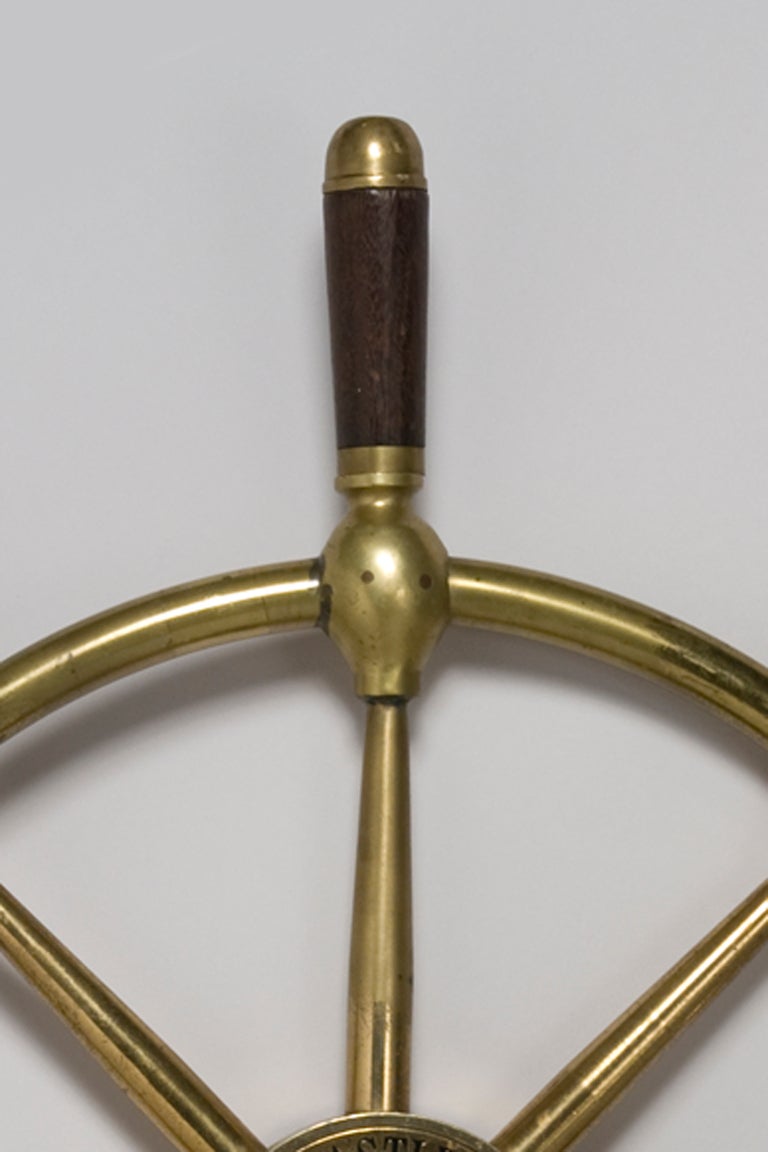 Bronze ship's steering wheel, eight arms emanating from the center circle, mahogany handles, English 1950s. Impressed around center 