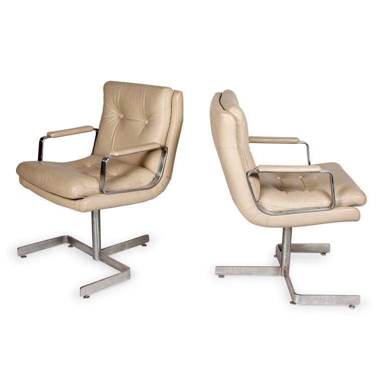 Pair of chrome and beige leather desk armchairs, seat on a central chrome column resting on U-shaped base, with button upholstery and leather armrests. By Raphael, French 1970s. Back height 33 in, seat height 19 in, width 22 in, depth 25 in. (Item