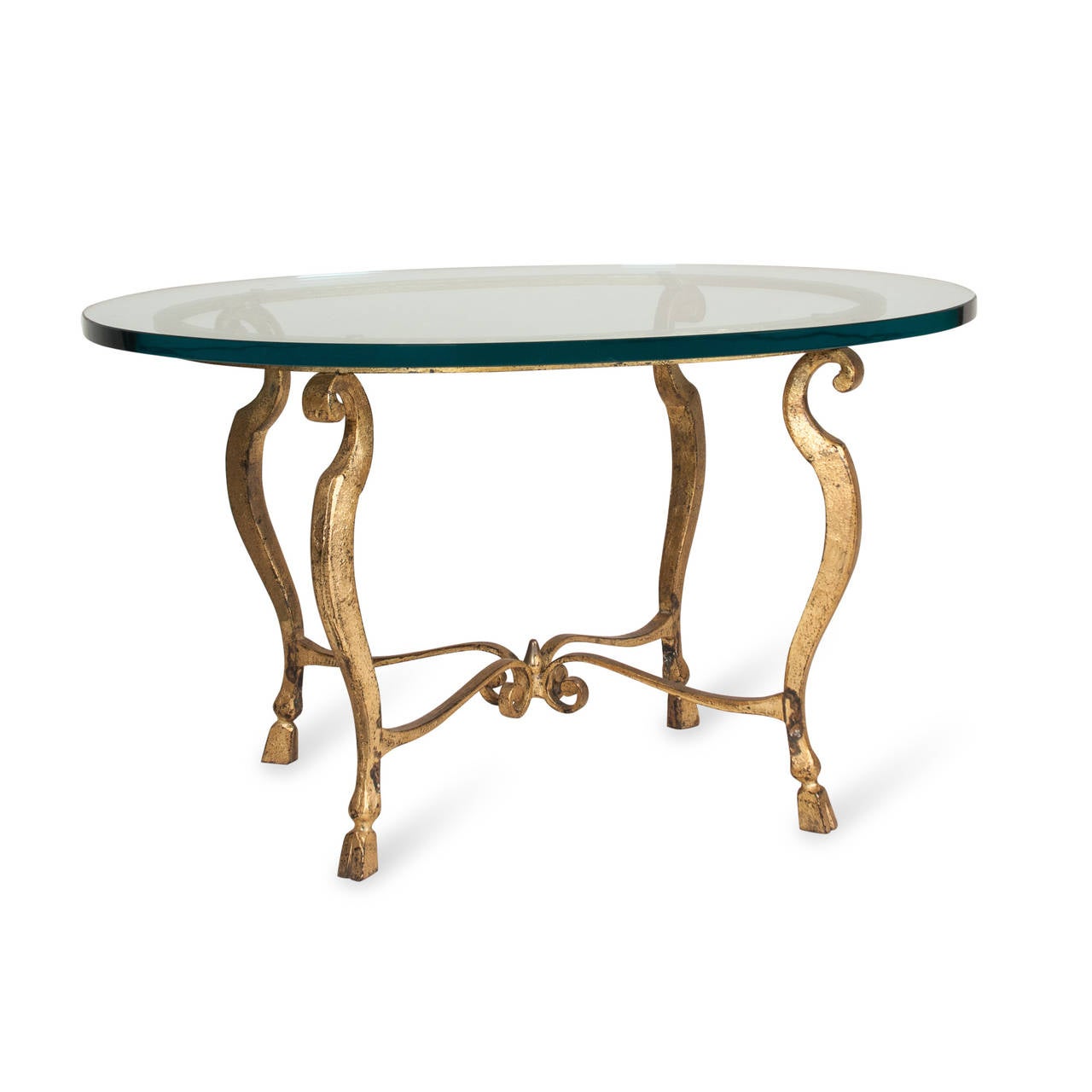 Gilt iron cocktail table, with oval starfire glass top, arced legs ending in hoof feet, center cross stretcher with ribbon center, French, 1960s. Width 30 in, depth 18 in, height 24 in.