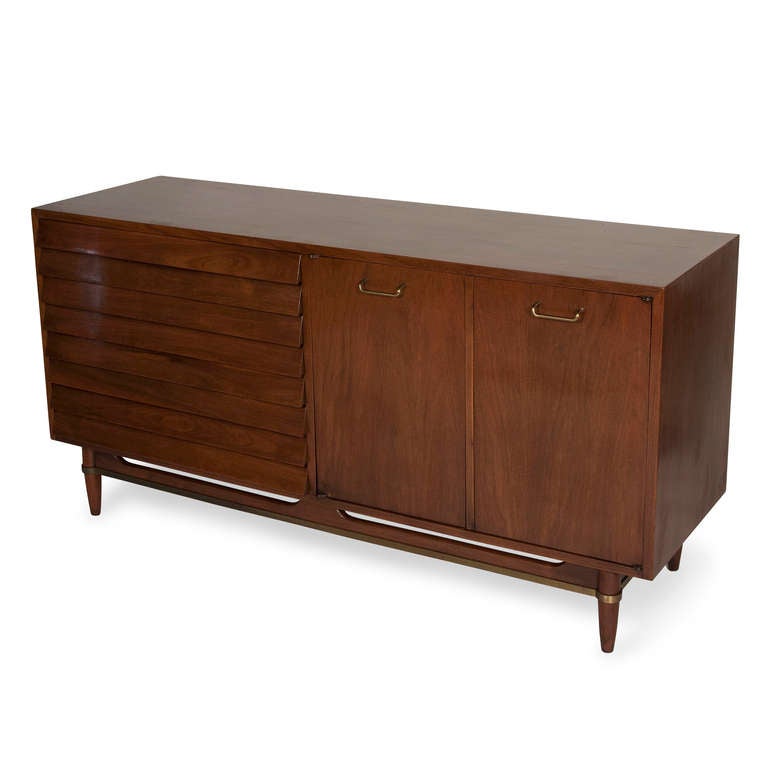 Walnut two door and drawer credenza cabinet, the two doors on right opening to reveal a small shelf compartment space and three melamine faced drawers, the left side having three slatted face drawers, the case raised on four legs with cross