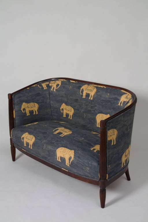 Elegant art deco two person settee, the acajou frame having fluted and tapered legs, the top of the curved back framed in wood, upholstered in Kravet cotton blend elephant print fabric, French 1930s. Width 46 in, depth 25 in, back height 30 in, seat