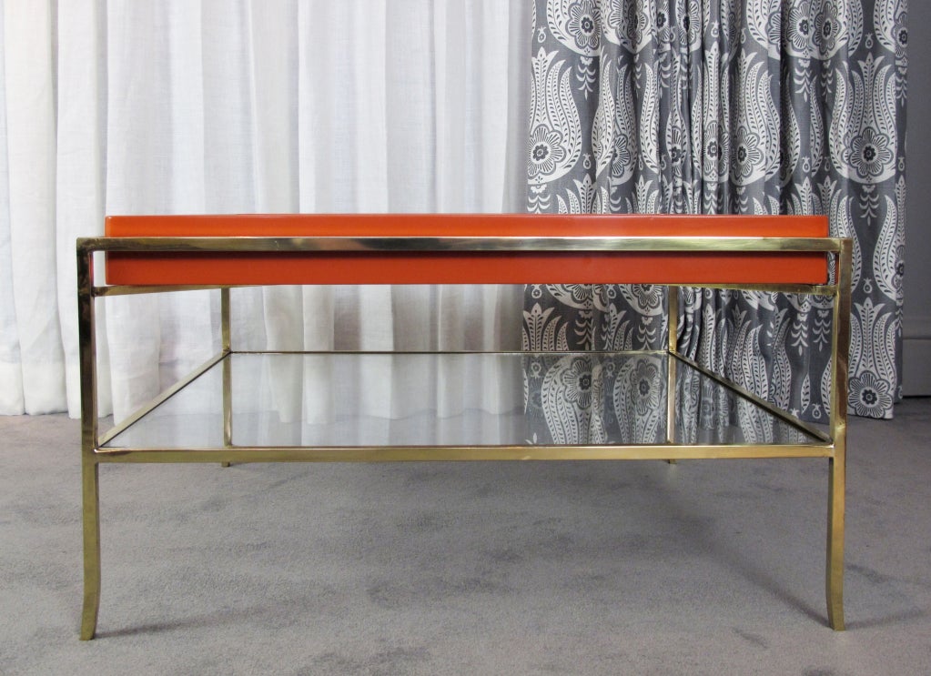 This is a rare cocktail or coffee table designed by Tommi Parzigner for Parzinger Originals.  Removable square lacquered tray rests in the brass structure.  Table has lower glass shelf.  Brass has been polished and lacquered.  The wood tray has been