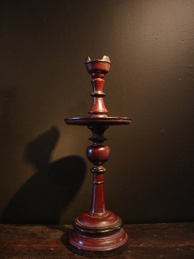 A pair of turned wood and lacquered candle sticks.

The elegant columnar, tapered bodies sit on rounded pedestal bases. An oversize circular drip pan has been placed 3/4 way up the body. 

The candle sticks are covered in red lacquer, with