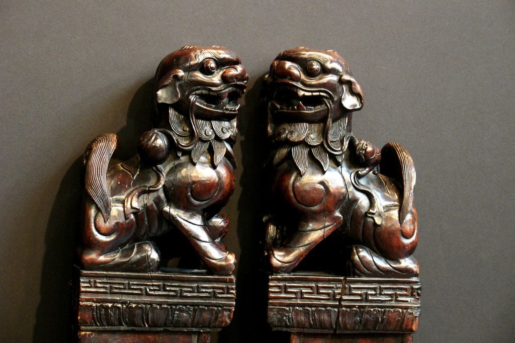 A charming pair of carved rosewood foo lions (aka foo dogs) set atop decorative carved columns. Originally used as architectural elements, most likely in a door way. Each lion holds a large, loose rosewood pearl in its mouth.  The rosewood has a