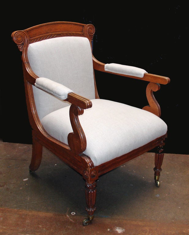 An elegant, simply carved oak open-arm library chair with a generous seating depth. The front legs are cylindrical and fluted while the back legs are simple saber legs. All sit on brass casters.