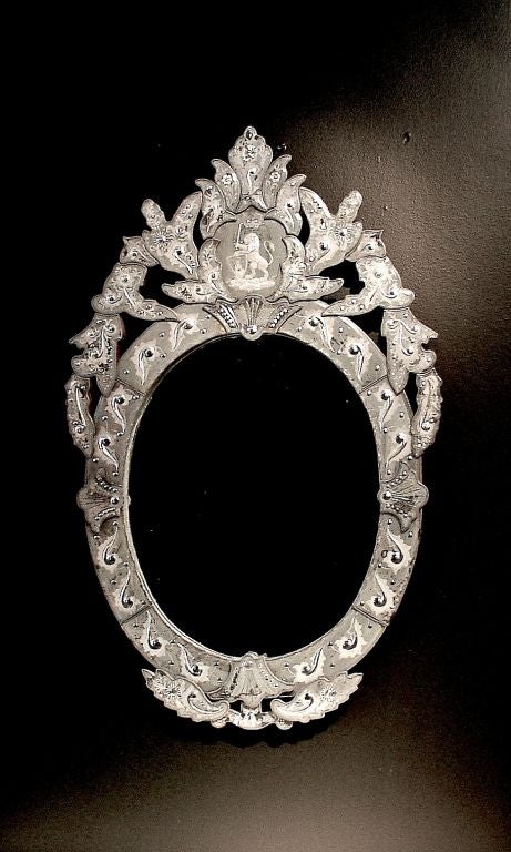 A Venetian glass wall mirror featuring a frame of hand cut, beveled and polished silvered glass. Further embellished with etched designs throughout. All surrounding an oval center mirror.