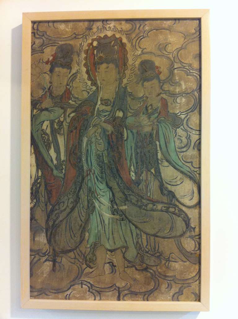 A Ming Dynasty Buddhist fresco featuring an image of the Bodhisattva Guanyin flanked by two attendants, all standing on a bank of clouds. The trio are depicted with full, round faces, dressed in loose, flowing robes and billowing capes, their hair