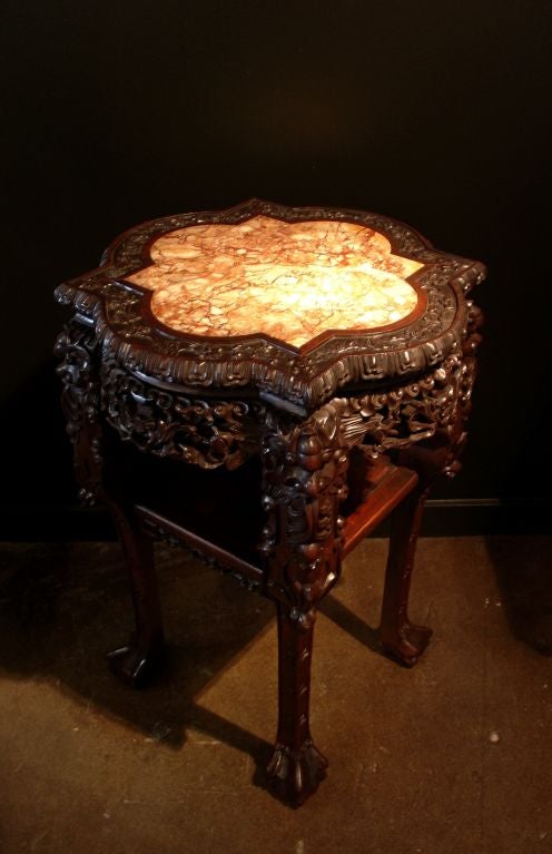 A heavily carved Chinese export quatrefoil table of hongmu (blackwood) with a marble inset top of pink variegated marble. Carved floral and foliate designs representing the four seasons surround the marble top. Carved lotus petals decorate the