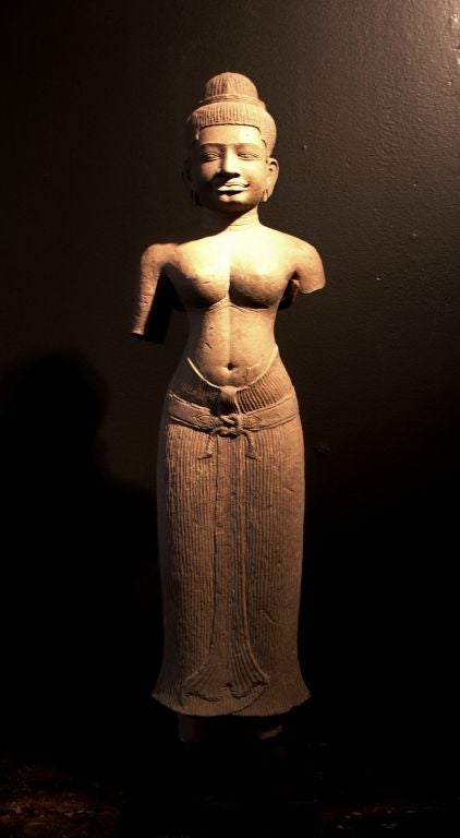A wonderfully sensual Khmer statue of a female divinity delicately carved from gray sandstone.

Her face radiates a cool serenity. Almond shaped eyes gaze out eternally from under a slightly arched and clearly defined brow. A prominent nose sits