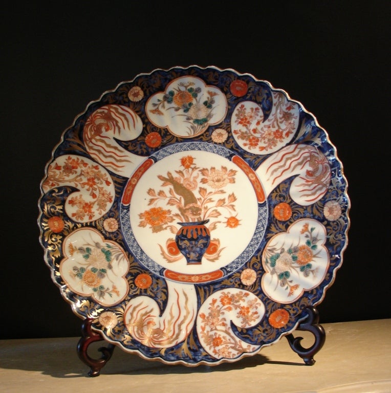 A large and fine Japanese porcelain charger with a fluted body and scalloped edge. 

The central medallion features an animated shi shi lion leaping into a vase of floral sprays. The surround is decorated with quatrefoil and paisley cartouches