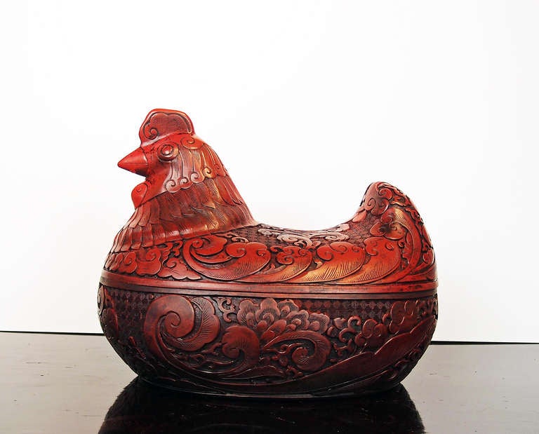 A finely carved cinnabar lacquer covered box in the form of a roosting hen.

The cinnabar lacquer is carved in fluid detail. While the heads of the hens are realistically portrayed, the wings, tails, and feathers are carved in an abstracted