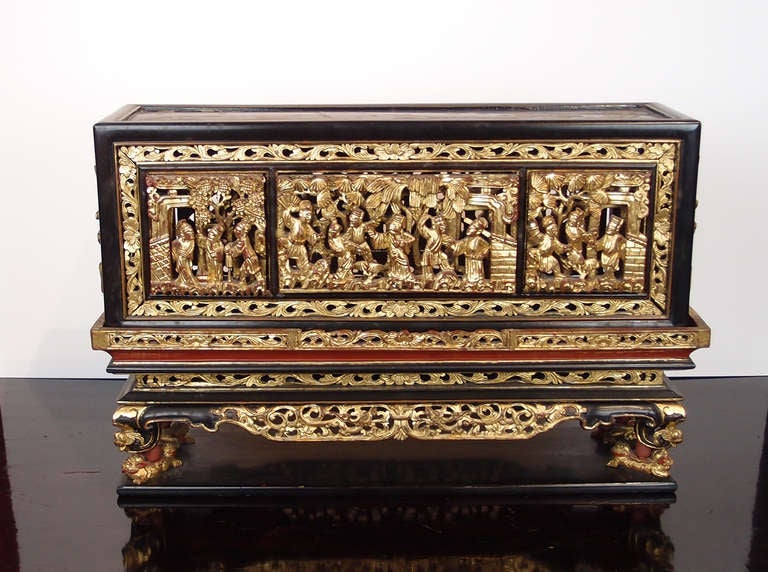 An intricately carved, lacquered, and gilt Chinese temple box. The lid featuring scenes of officials in a courtyard setting, and floral decorations to the top and sides. The base of altar form, raised on four foo lion shaped feed, carved with