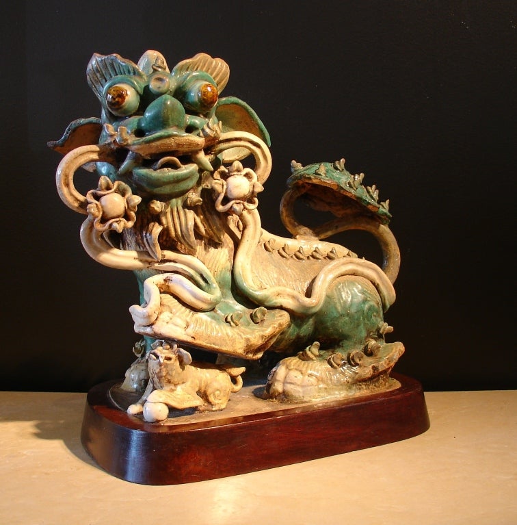 A large shiwan pottery figure of a frolicking female foo dog. She carries a streaming ribbon in her slightly opened mouth, while a cub plays underfoot. Her long, bushy tail has been shaped as a ruyi. Bulging eyes and oversized ears give her a