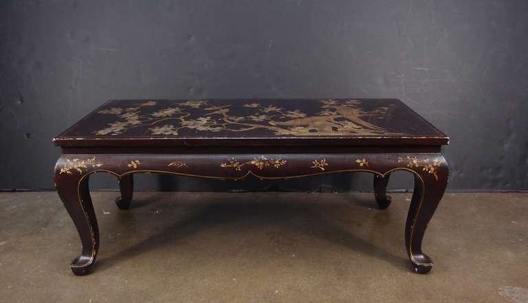 An attractive French chinoiserie brown lacquer coffee or cocktail table with gilt painted decoration, circa 1940's, France. 

Set upon graceful cabriole legs and draped apron, the top has been parcel-gilt with a design of two long tailed birds
