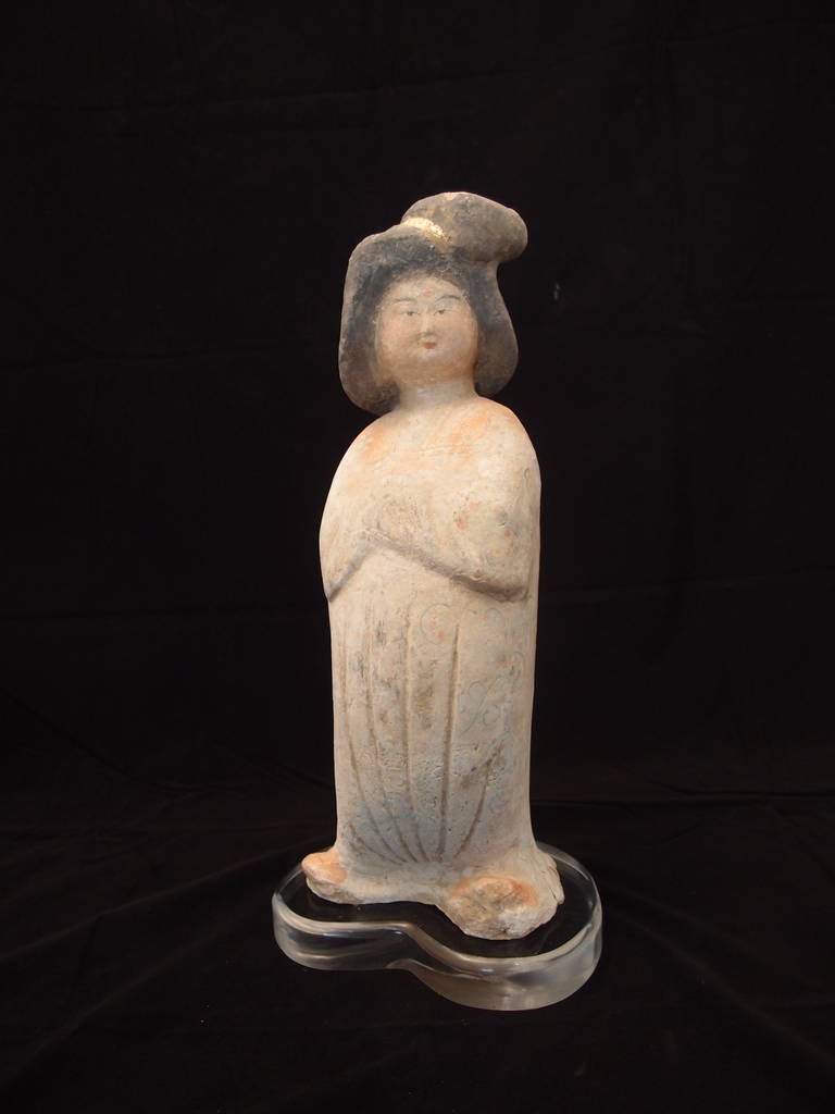 Painted pottery figure of an opulent Chinese court woman with up-swept hair and standing in a simply draped robe from the Tang Dynasty (618-907 AD). Her beauty is illuminated by the remaining painted imagery on her face, robe, and a gilded comb in