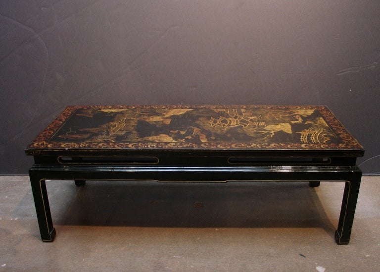 An elegant French black lacquer coffee table decorated in the Chinoiserie taste. 

A gilt painted landscape scene featuring a figures in a picturesque garden with willow trees, a moon bridge and pagoda, all set in a frame of scrolling acanthus