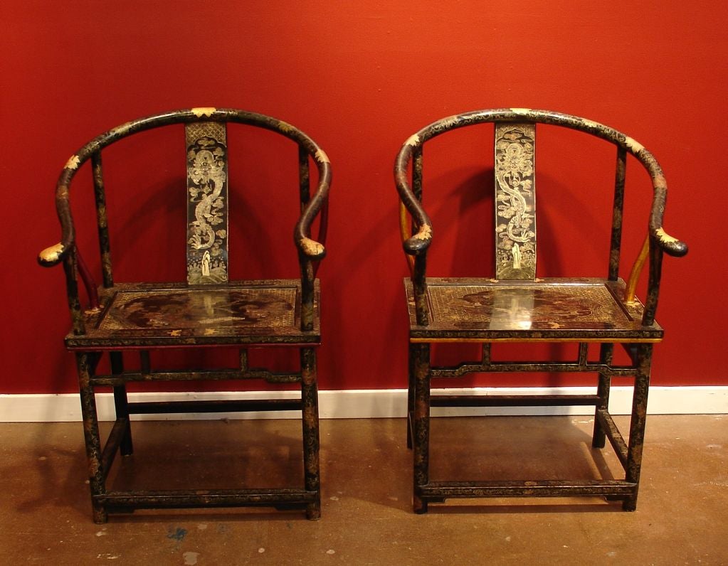 A pair of Chinese export painted and parcel gilt black lacquered horseshoe back arm chairs in the Chinoiserie style. <br />
<br />
The chairs are richly decorated all over with a floral and foliate design. Writhing five-clawed dragons rising above