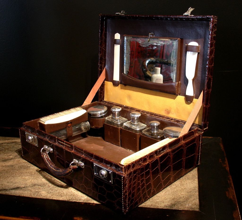 A gentleman's fitted traveling vanity case in brown alligator. The interior features a complete set of original accessories - six glass containers with silver lids, three ivory and horsehair brushes, folding mirror, an ivory shoehorn along with