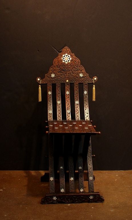 An ornately carved folding chair with mother of pearl and wood geometric inlay. Originally used by a traveling scribe, this chair is a wonderful marriage of functionality, comfort, and portability. An Arabic inscription graces the top.