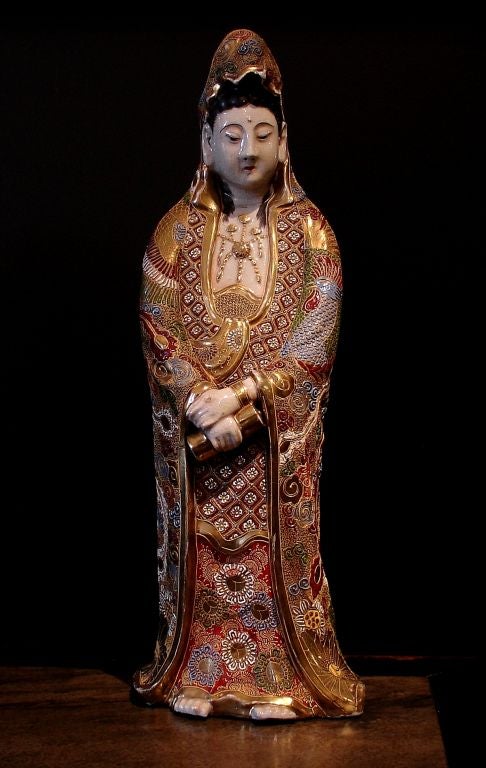 An large, finely molded and extensively decorated model of the Goddess of Mercy, Kannon Bosatsu. <br />
<br />
Her long flowing robes richly gilt and decorated in a floral and phoenix pattern of raised enamels. Her hands clasped in front of her