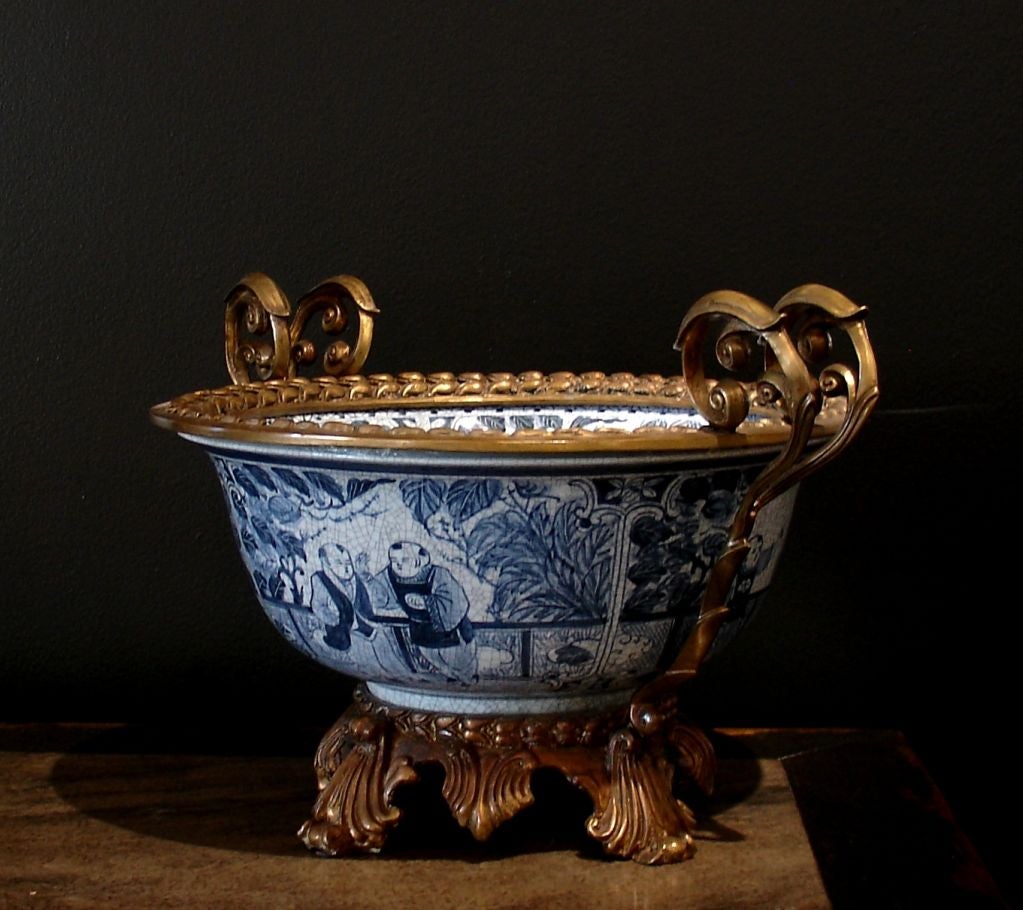 A large Chinese blue and white painted porcelain basin or punch bowl mounted as a center piece. The bowl features a crackle glaze and scenes of boys in a garden setting during the four seasons. The pomponne mounting features acanthus leaves for feet