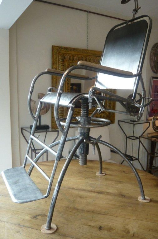 Polished Iron, fully retractable and adjustable medical chair with head rest, leg stirrups and wooden armrests.