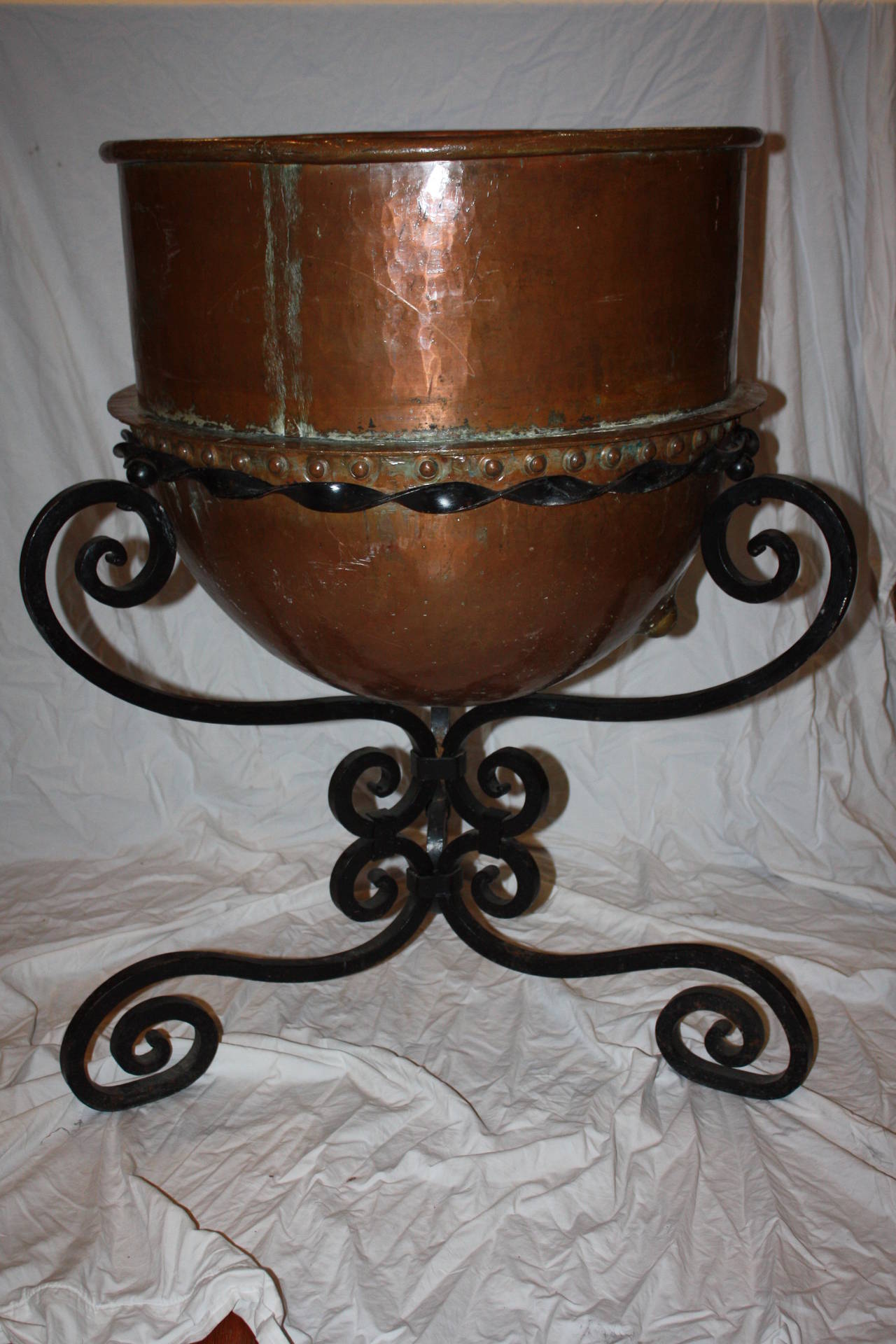 This is a very large copper pot on stand I purchased in France.  It would make a great log or kindling holder next to a fireplace. It would also make a very nice planter.  It is pierced by a hole that is part of the original design.  The wrought