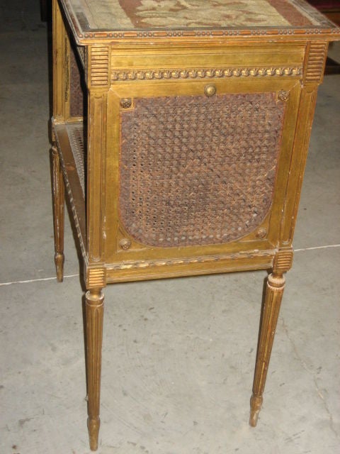 Beautiful gilded and carved Louis XVI side table.  This table has wonderful cane on both sides of the table and the bottom shelf. It has tapered fluted legs and carving around the table top. The top of this table is covered with a handmade tapestry
