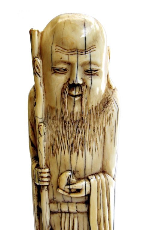 Most likely representing Shoulao, the figure well carved with a gentle expression, exaggerated domed head, and long incised beard, holding a gnarled staff in the right hand and a peach in the left, wearing long robes clasped in front and a cloth