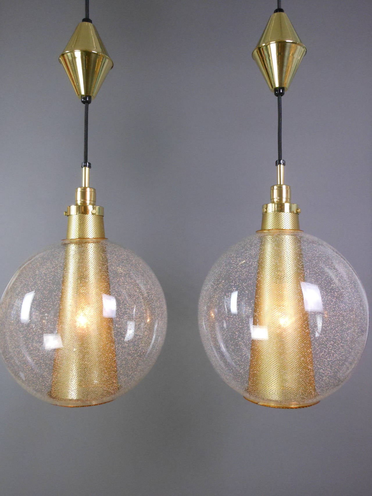 Each sphere, with small bubble inclusions throughout, centered by a perforated brass cone-form shade.