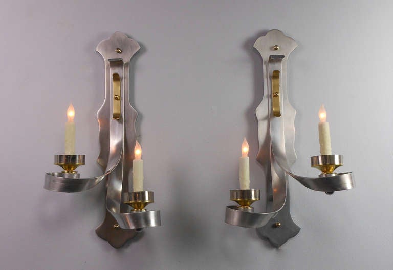 Each mid-century wall light has a vertical, shaped backplate issuing scroll arms fitted with circular candleholders.