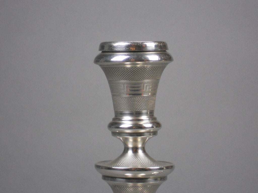 The Swedish silver candlesticks have an engine turned baluster stem surmounted by an urn form candleholder with a Greek key frieze, on a conforming circular socle and base.

Maker's Mark: LL& Co. (Lars Larsen & Co.)
National Mark: Swedish