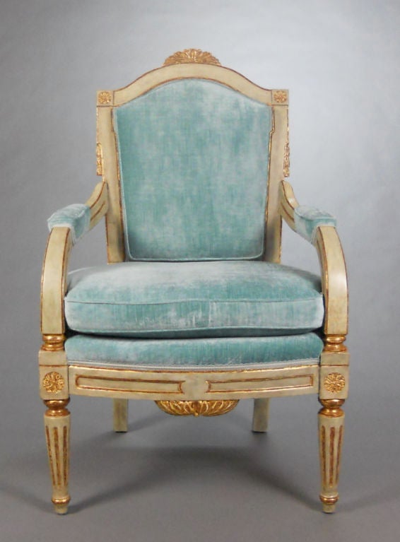 Each with an arched toprail surmounted by a foliate crest and flanked by paterae, the upholstered backrest above downswept fluted arms and the paneled bowfront apron, raised on sabre back legs and tapering fluted front legs.