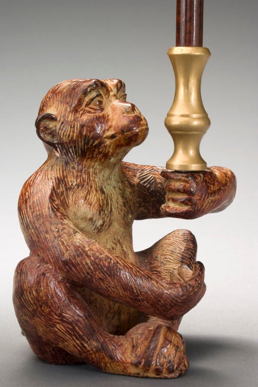 The seated monkey holds a trumpet blossom candleholder atop a column.