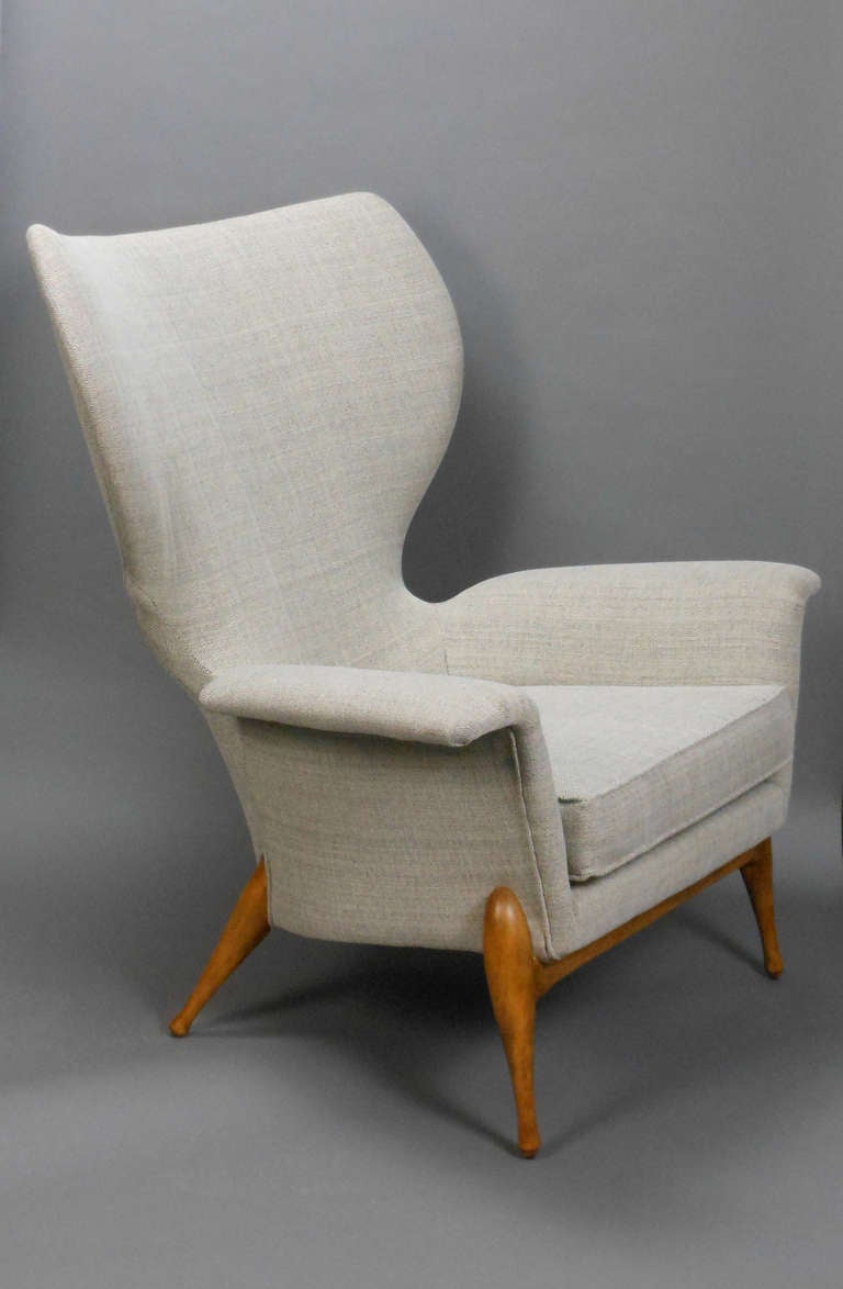 The curved backrest with eared corners and outswept arms, on circular tapering legs.