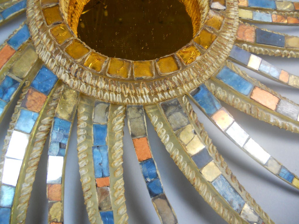 The circular amber tinted mirror plate within the stepped molded frame inset with conforming squares, radiating an asymmetric pattern of curved rays adorned in a polychromatic glass mosaic.