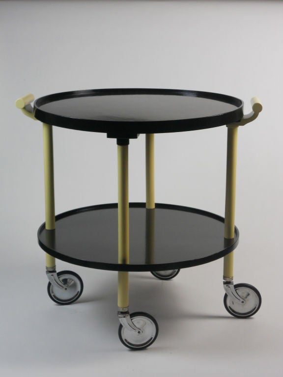 The circular tray top fitted at the sides with scroll handles, on four column supports above a conforming lower tier and ending in wheels. Each wheel stamped OPAL-SCHLEIFLACK D.R.G.M.