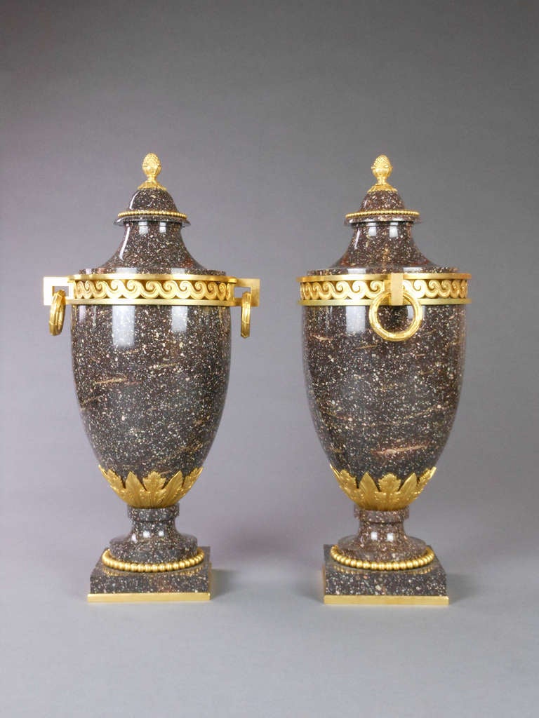 These spectacular Blybergs porphyry urns are mounted with a foliate frieze and a pierced Vitruvian scroll frieze. The square handles are hung with beribboned wreaths. The stepped, cupola form covers are fitted with a beaded frieze and surmounted