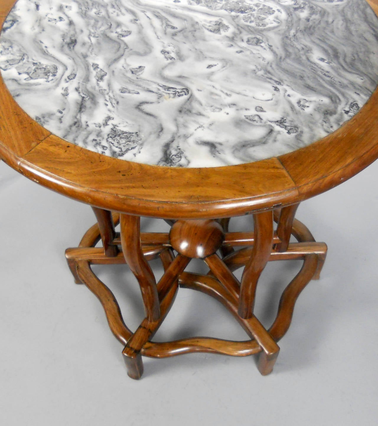 This Qing dynasty circular table has a beautiful grey, black, and white marble top set within a hardwood frame. The six curvilinear legs are connected by a sunburst stretcher raised on an open hexafoil base.