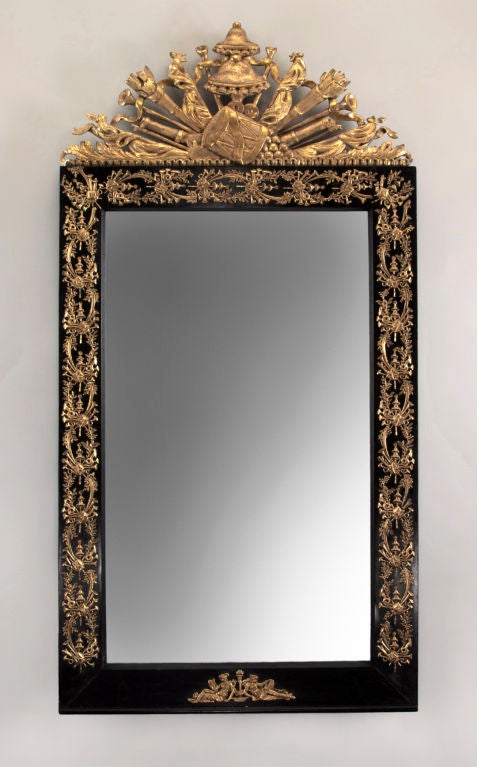 The rectangular mirror plate within the conforming frame mounted with foliate and musical motifs, the base with adorsed classical female figures, surmounted by a trophy including trumpets, furled flags, and a drum beneath a chapeau de chinois.