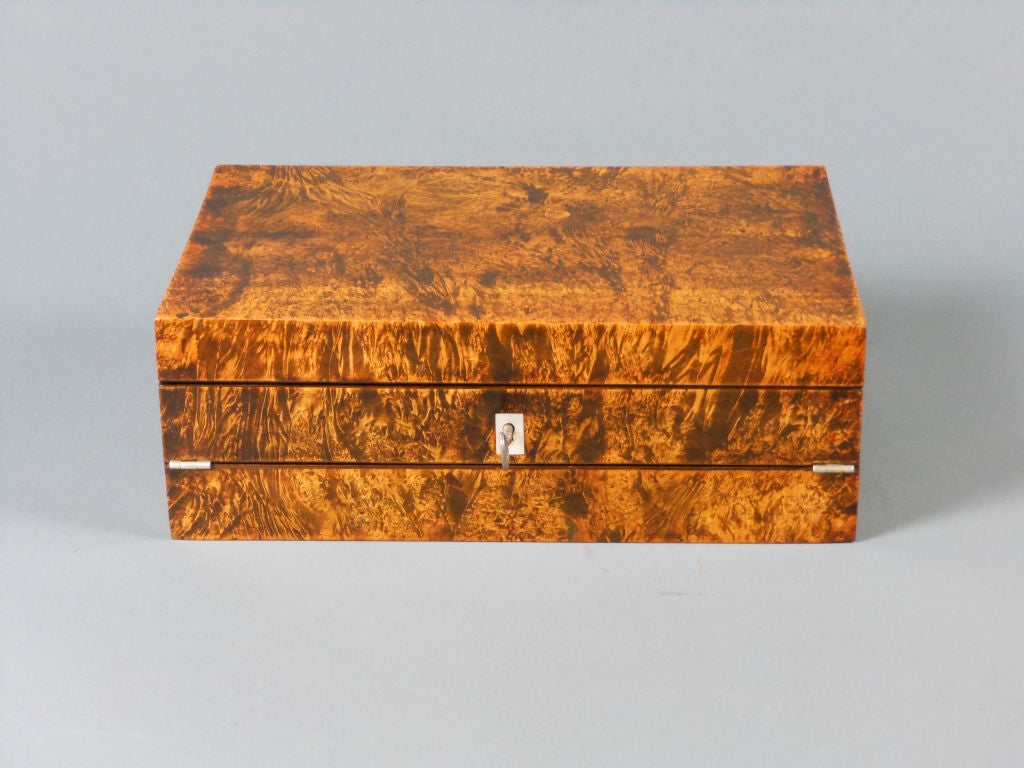 The whole with richly figured continuous burl veneer, the rectangular lid with leather pocket opening to reveal a hinged velvet-lined writing surface, pen tray and two inkwell compartments, the tray opening to another compartment. <br />
Labeled