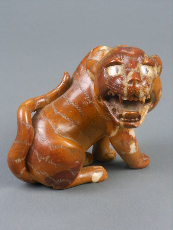 The expressive, growling tiger is seated on its haunches with its head turned to the side and an upturned tail resting on its back. The surface is incised with tiger stripe markings.