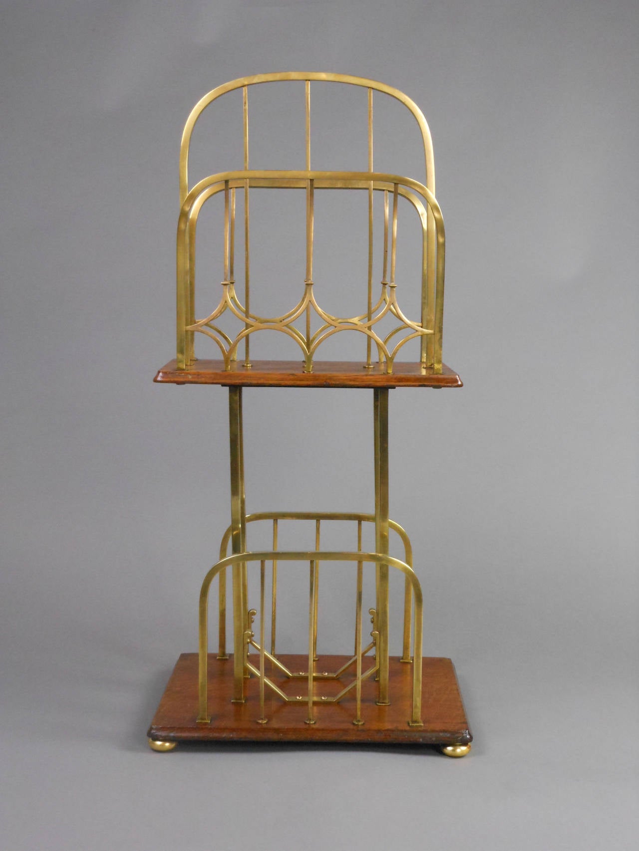 The Arts and Crafts period magazine rack has two oak shelves fitted with brass arched grills and bun feet.