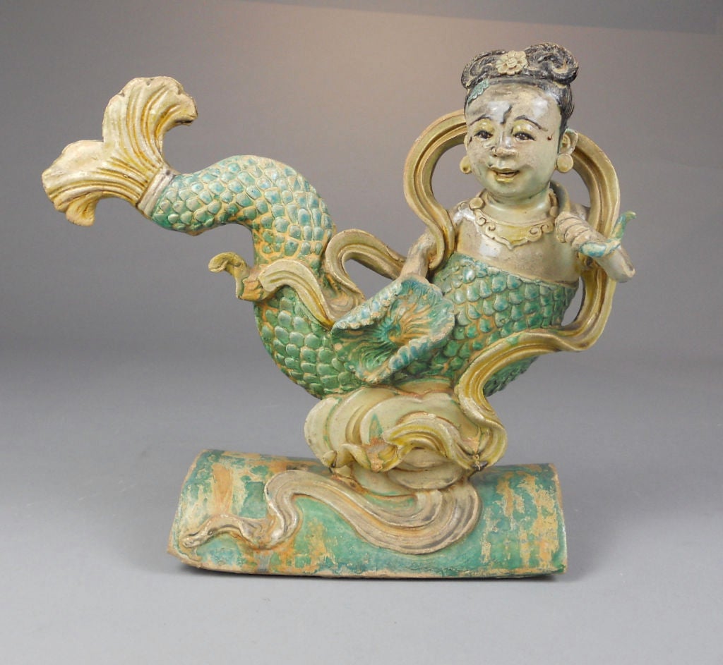 Seated on stylized waves with upturned serpentine tail and holding a lotus flower.