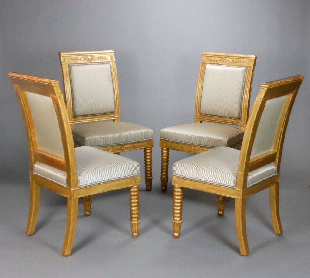 Each with a rectangular upholstered backrest with a fluted border and surmounted by a toprail centered with a Mercury mask, the trapezoidal seat above the apron with a paterae issuing a foliate frieze, raised on turned front legs ending in fluted