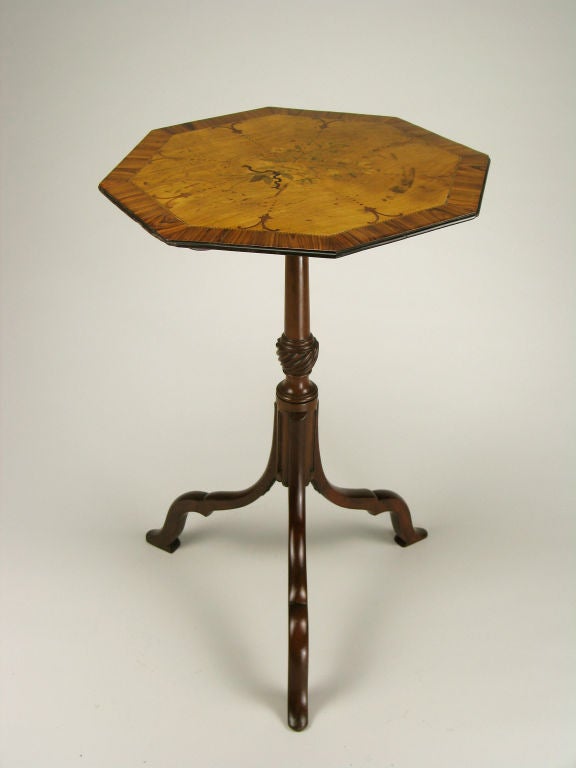 The octagonal satinwood top centered by a beribboned spray of flowers within a stringed and crossbanded kingwood border, the spiral carved and fluted yew wood center pedestal above the three bloodwood scroll legs ending in stylized hoof