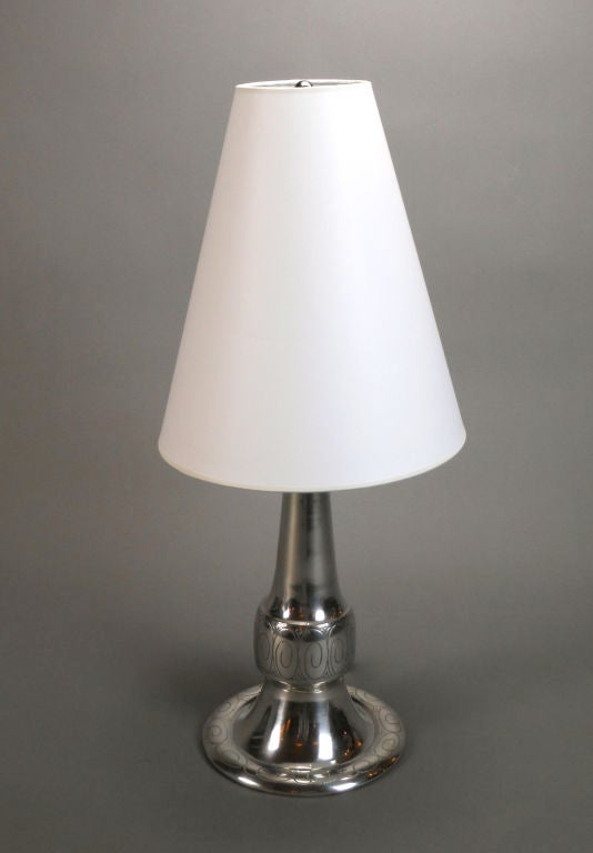 This Swedish table lamp has a tapering cylinder form centered by a convex band with incised scroll decoration, with a conforming circular base.  Stamped SVENKST Cela. TENN.6

Height to base of light socket: 11"
Height to top of finial: 22"