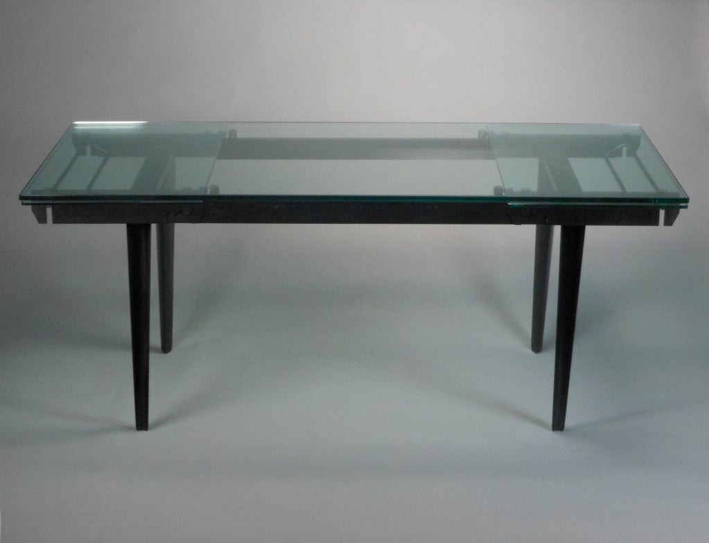 The rectangular top above the black frame raised on four tapering, rounded, triangular legs. Table extends to 109.5