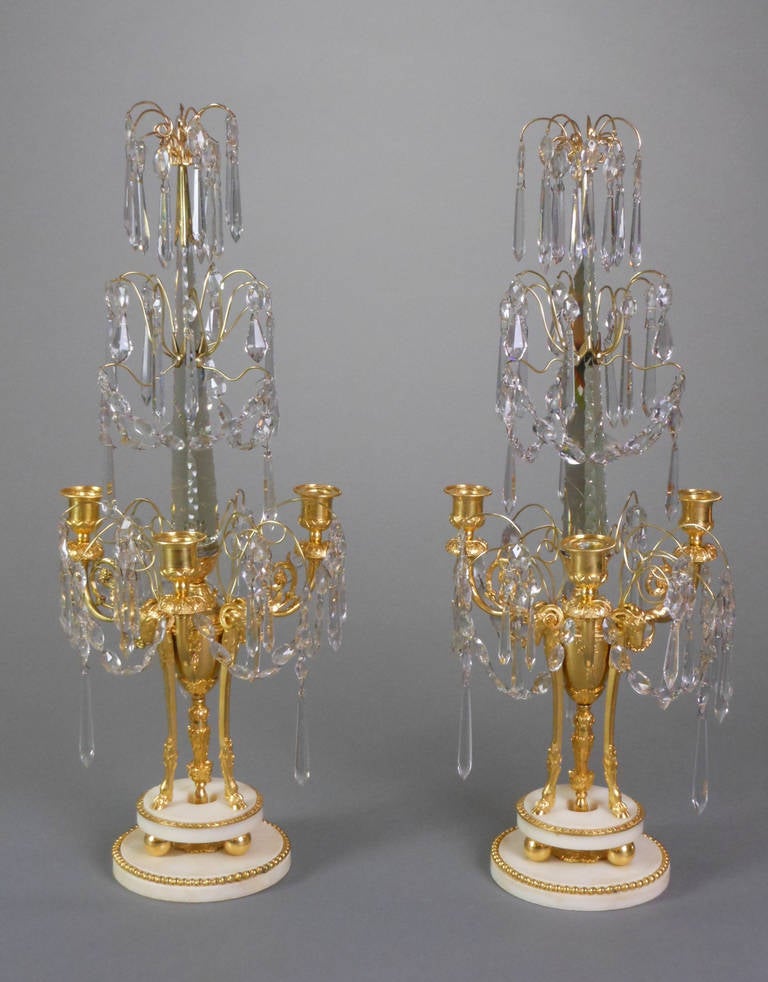 Each candelabrum has a tripod censer mounted with ram's heads and issuing three foliate scroll arms hung with garlands and ending in an urn form candleholder. The notched obelisks are fitted with sprays of crystals. The circular bases are stepped